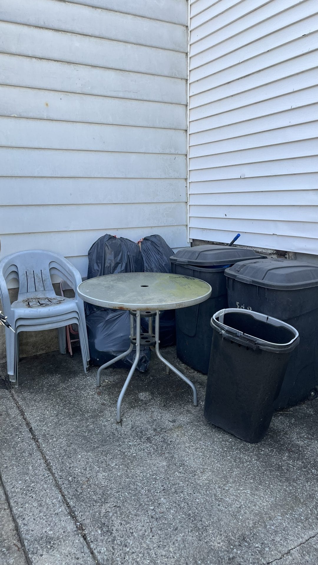 Plastic chairs and trash bags stacked against the side of a house